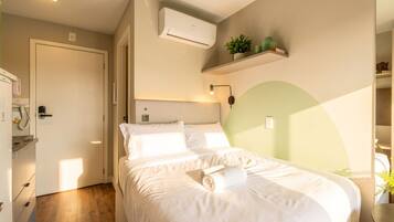 A bedroom with a bed, a bedside table, a wall-mounted air conditioner, and a shelf with decorative items.