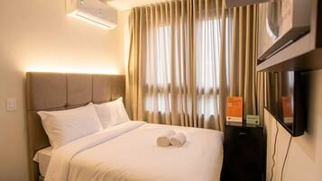 A hotel room with a bed, a TV, and a wall-mounted air conditioner.