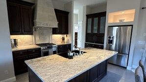A modern kitchen with dark cabinetry, a large island, stainless steel appliances, and a marble countertop. - Idaho Falls 6bed4bath Exquisite Home (Idaho Falls)