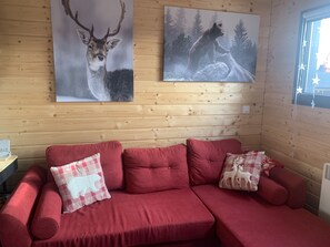En röd soffa med tillhörande kuddar, två inramade djurmotiv på väggen och ett fönster dekorerat med stjärnor.