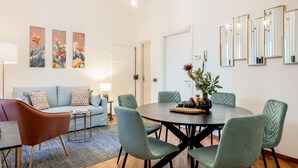 A modern living room with a round dining table, teal chairs, a sofa with patterned cushions, and wall-mounted mirrors. - Genteel Home Contessa Matilde (Pisa)