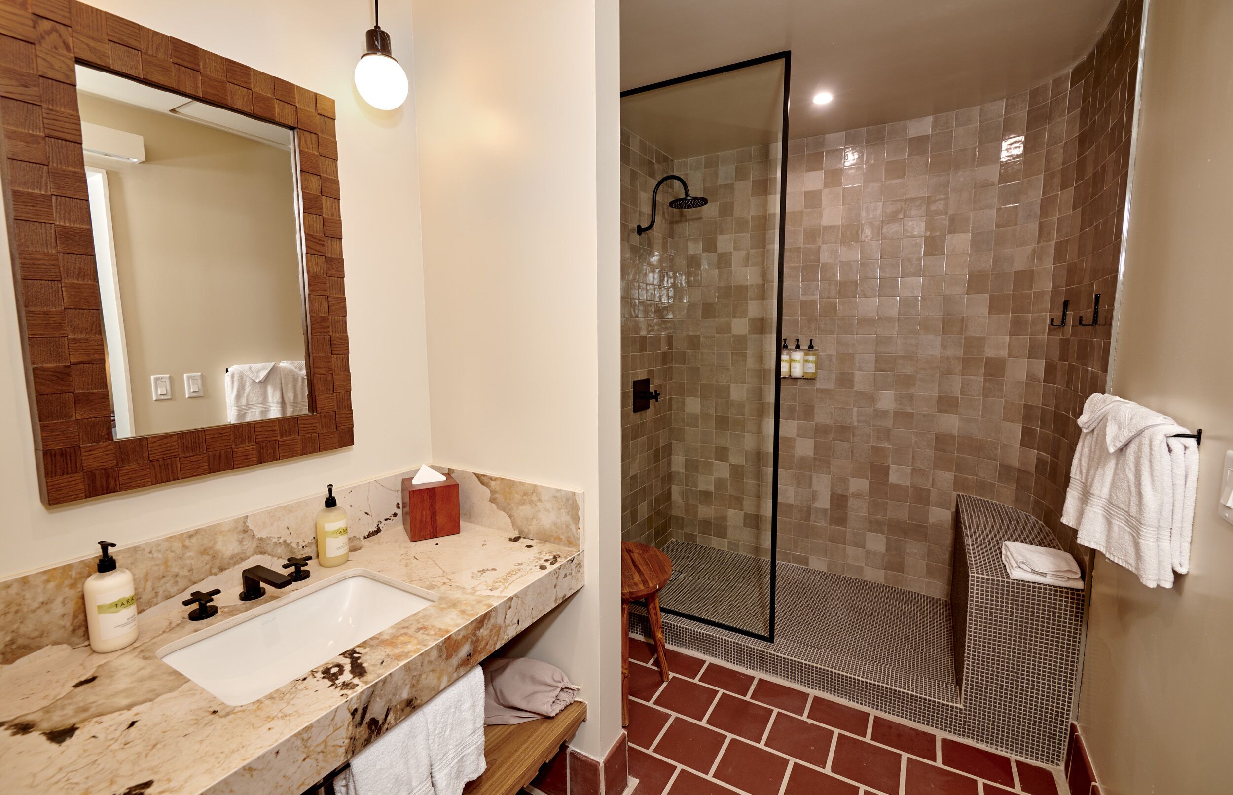 Une salle de bain dotée d’un lavabo en marbre, d’un miroir encadré en bois et d’une douche à parois de verre, les murs étant recouverts de carreaux.