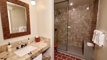 Une salle de bain dotée d’un lavabo en marbre, d’un miroir encadré en bois et d’une douche à parois de verre, les murs étant recouverts de carreaux.