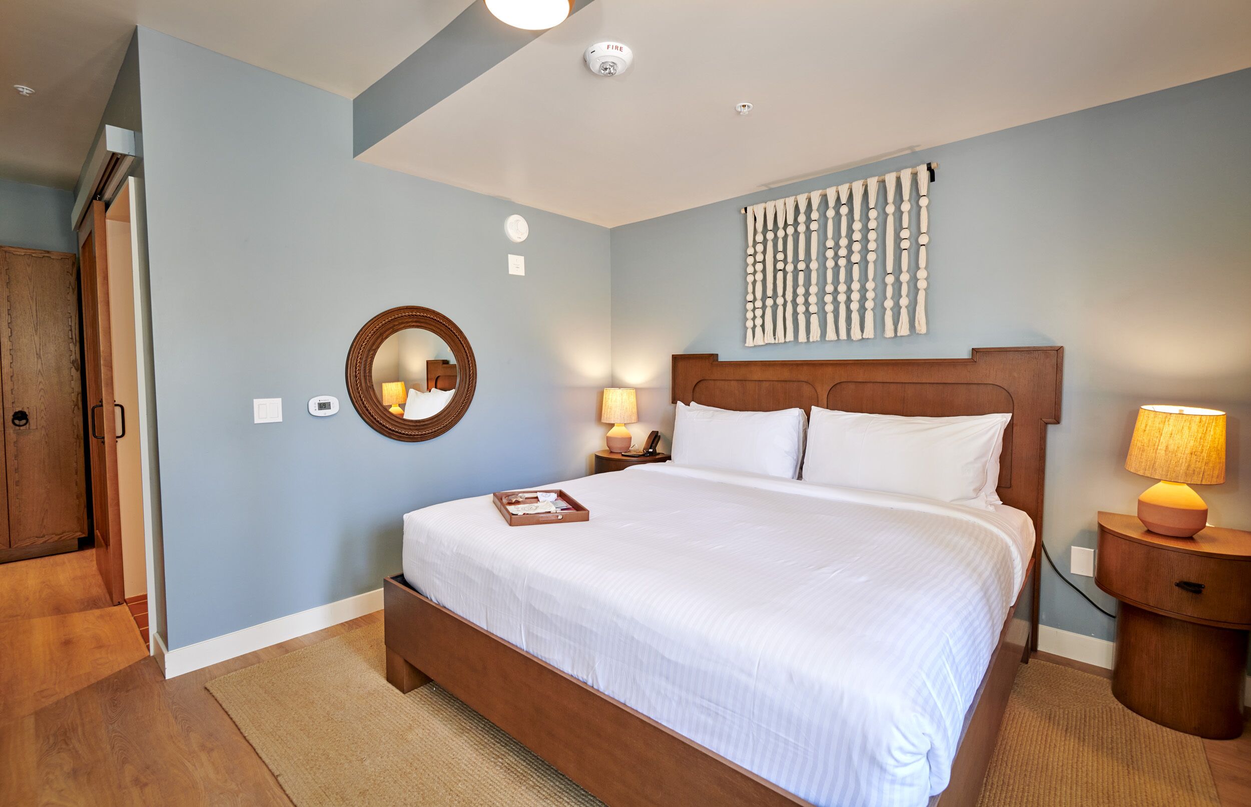 A bedroom with a large bed, a wooden wardrobe, a round mirror, and a wall-mounted artwork.