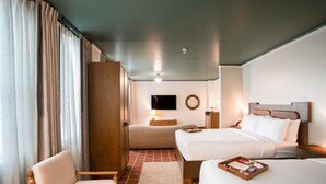 Una habitación de hotel con dos camas, un armario de madera, una silla, un televisor en la pared y una mesita de noche con una lámpara.