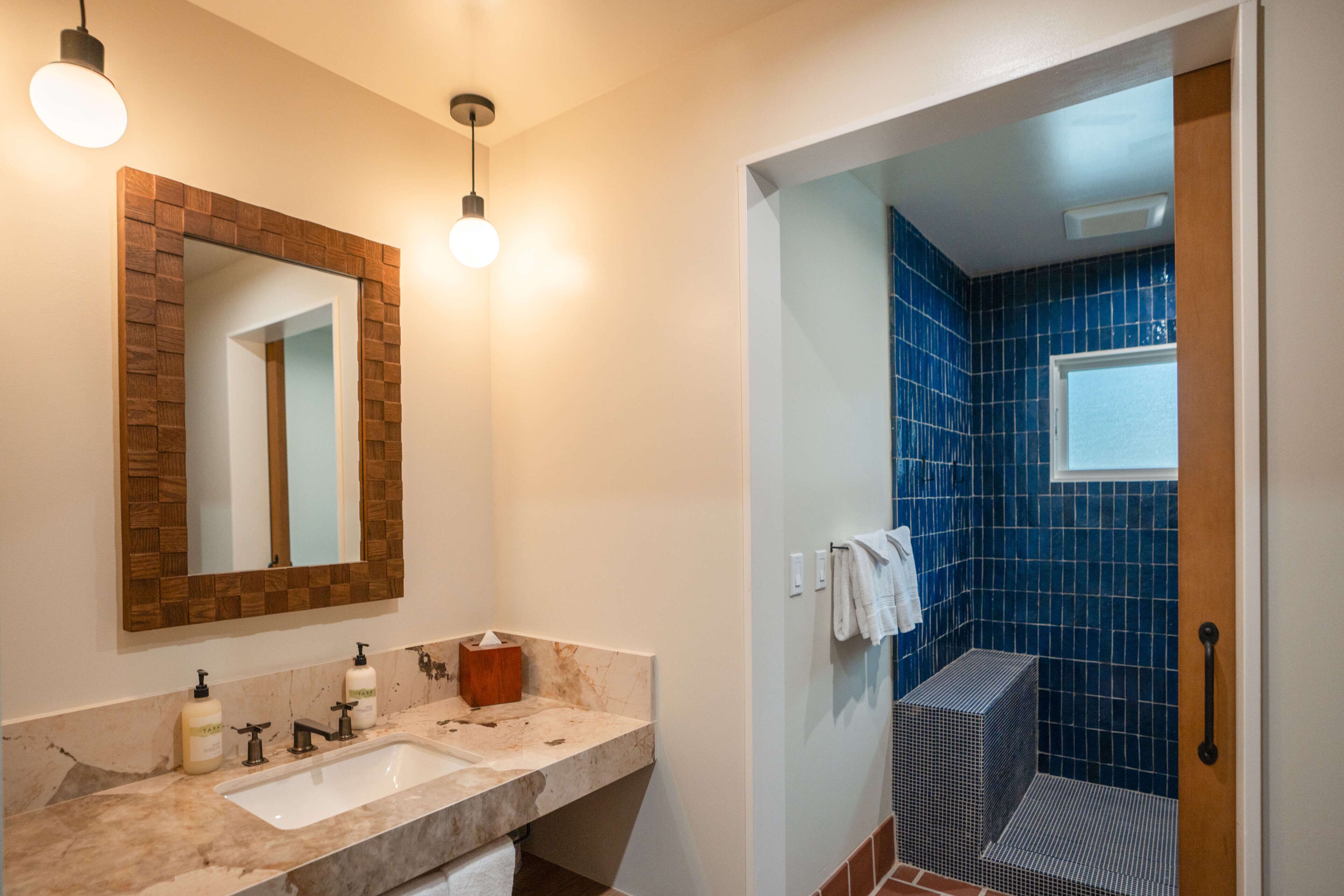 Um banheiro com pia de mármore, espelho com moldura de madeira e área de chuveiro com azulejos azuis.