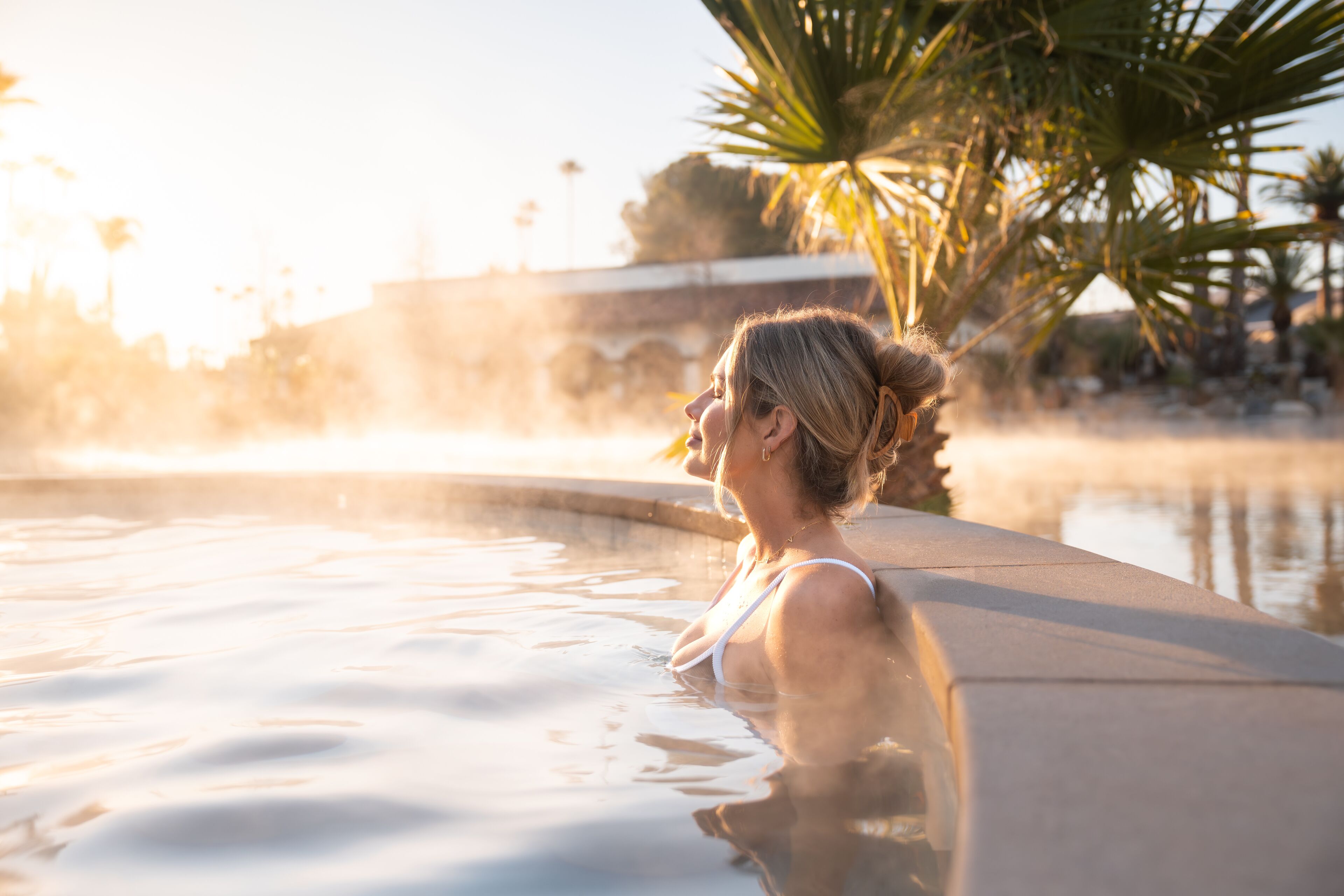 A person in a swimming pool with a clear view of the pool's edge and surrounding palm trees.