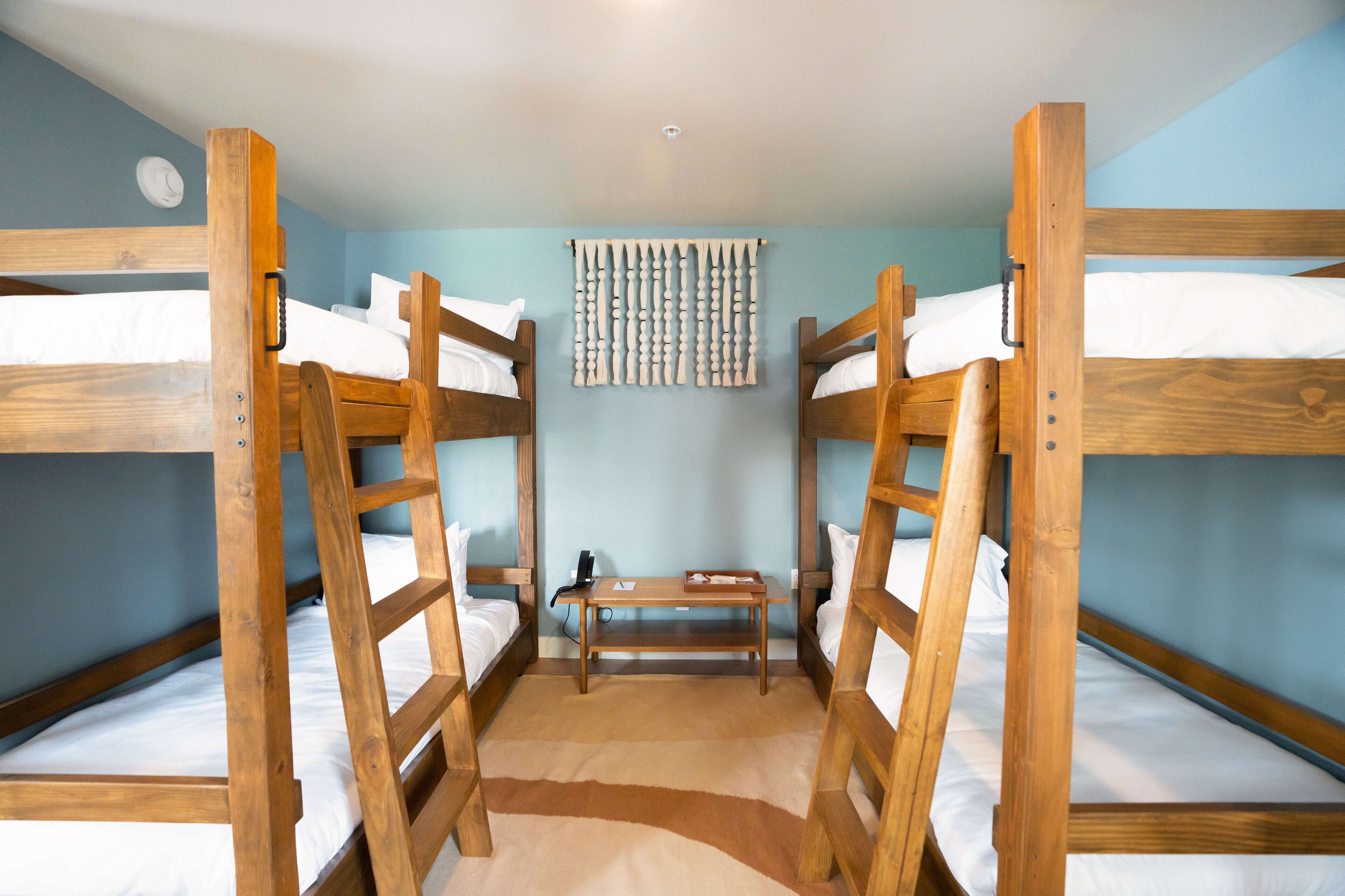 Habitación con literas, una escalera de madera, una mesita pequeña y una cortina instalada en la pared.