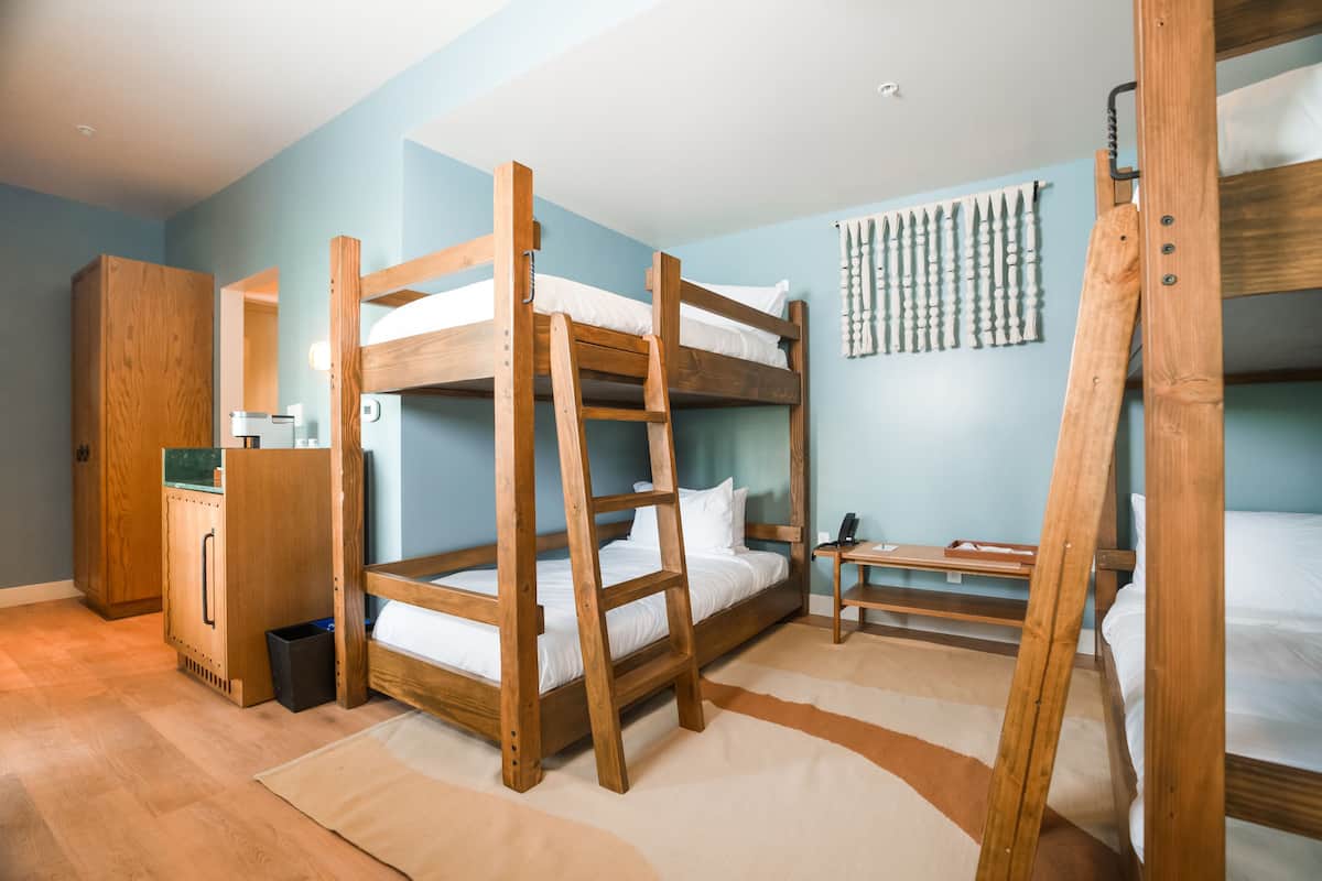 A bunk bed room with a wooden ladder, a desk, and a wardrobe.