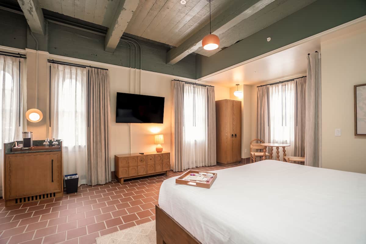 A hotel room with a large bed, a wooden dresser, a television mounted on the wall, and a small table with chairs.