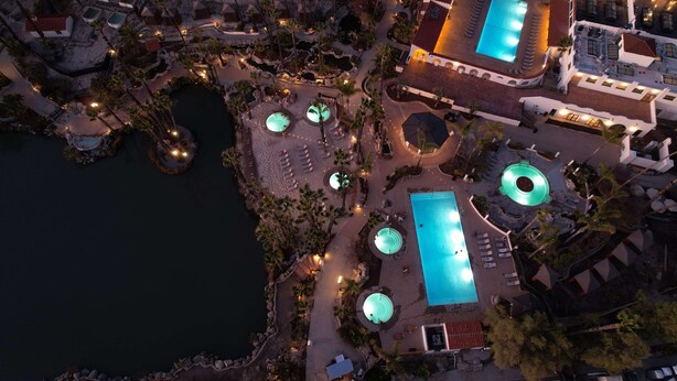Vista aérea de un resort con múltiples piscinas, palmeras y zonas de descanso en la playa.