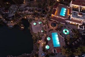Vista aérea de un resort con múltiples piscinas, palmeras y zonas de descanso en la playa.