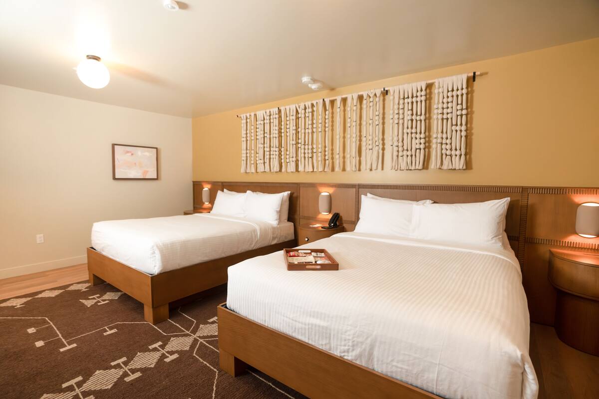 A hotel room with two beds, a patterned rug, and wall-mounted lamps.