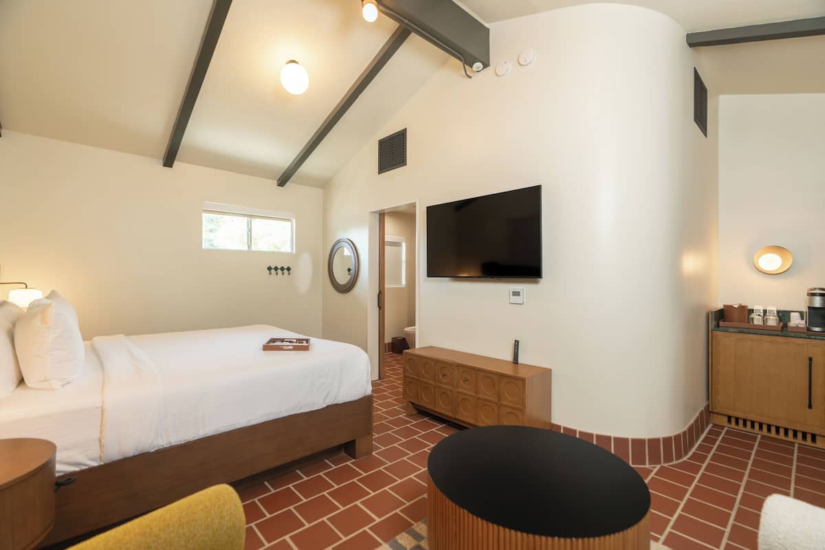 A modern hotel room with a bed, a TV, a wooden cabinet, and a brick-patterned floor.