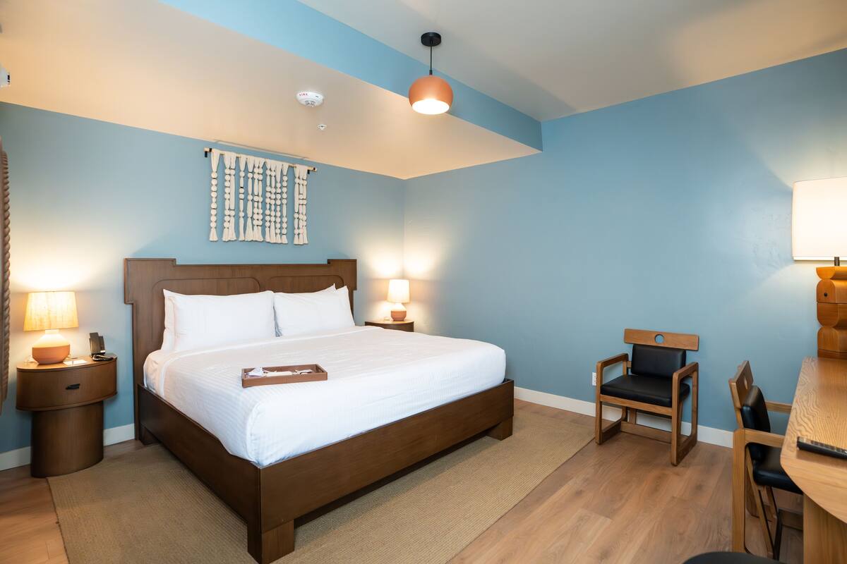 A bedroom with a large bed, two bedside tables with lamps, a wooden chair, and a small table.