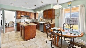 A spacious kitchen with wooden cabinets, a central island, and a dining area with a table and chairs. - New! Spacious 3K sq ft 4BD/3Bath + Pool (Bakersfield)