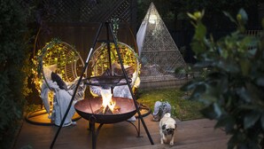 A fire pit with a hanging chair and a decorative cone structure in a garden setting. - Romantic Lodge on Edge of Nature Reserve (Colchester)