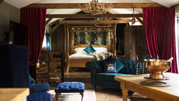 A rustic bedroom with a wooden bed, a green sofa, and a wooden table. - Romantic Lodge on Edge of Nature Reserve (Colchester)