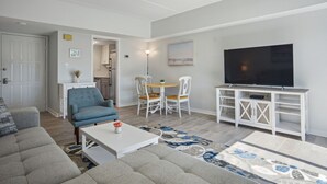 A modern living room with a grey sofa, a blue armchair, a white coffee table, and a TV on a white stand. - Totally Renovated 1BR/1BA/All New Furniture/Sofa Bed/Balcony/Walk-In Shower/WiFi (Hilton Head Island)