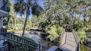 A wooden bridge over a pond with surrounding trees and a building with a balcony. - Totally Renovated 1BR/1BA/All New Furniture/Sofa Bed/Balcony/Walk-In Shower/WiFi (Hilton Head Island)