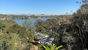 Une vue sur un lac, avec une ville en arrière-plan, entourée d’une végétation luxuriante et un bâtiment à la façade blanche.