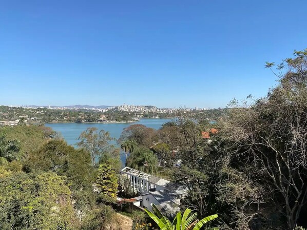 A view of a lake with a city in the background, surrounded by dense greenery and a building with a white facade.