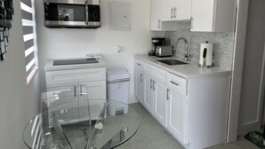 Una cocina moderna con armarios blancos, electrodomésticos de acero inoxidable y una mesa de comedor con cubierta de vidrio.