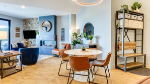 A modern living room with a round dining table, comfortable seating, a stone fireplace, and a bookshelf with storage boxes. - Downtown Winter Park Condo: Steps to Everything! (Winter Park)