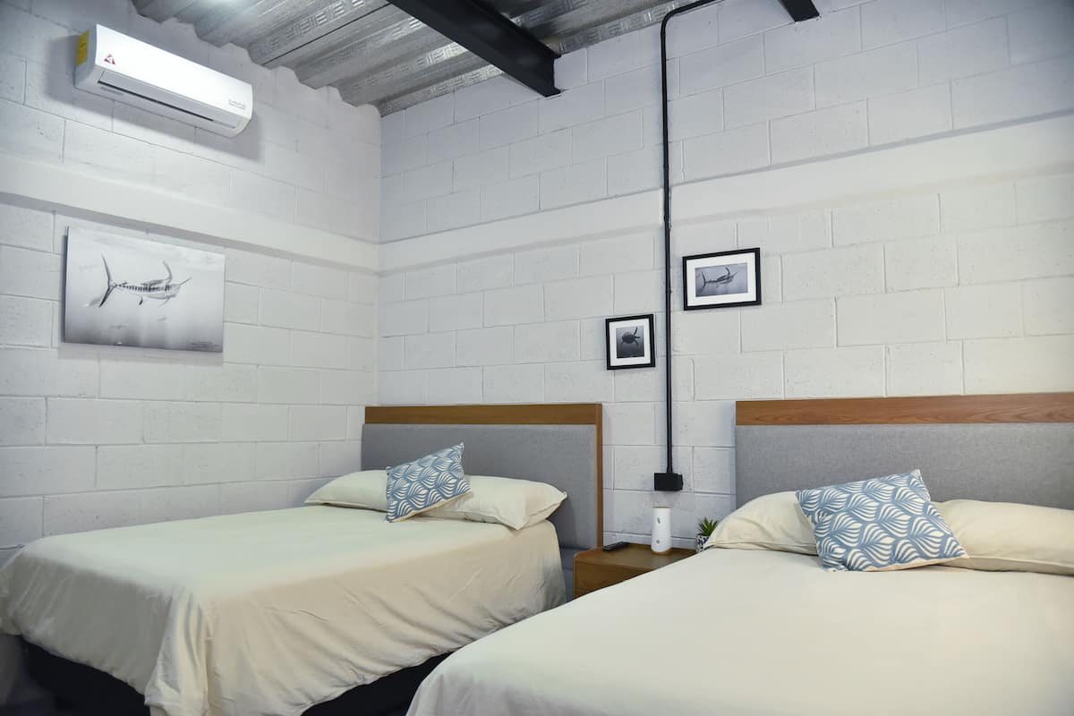 A room with two beds, white brick walls, and a ceiling with exposed beams.