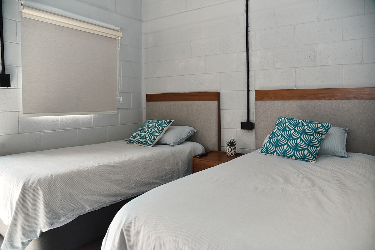 A hotel room with two single beds, white bedding, and patterned pillows.