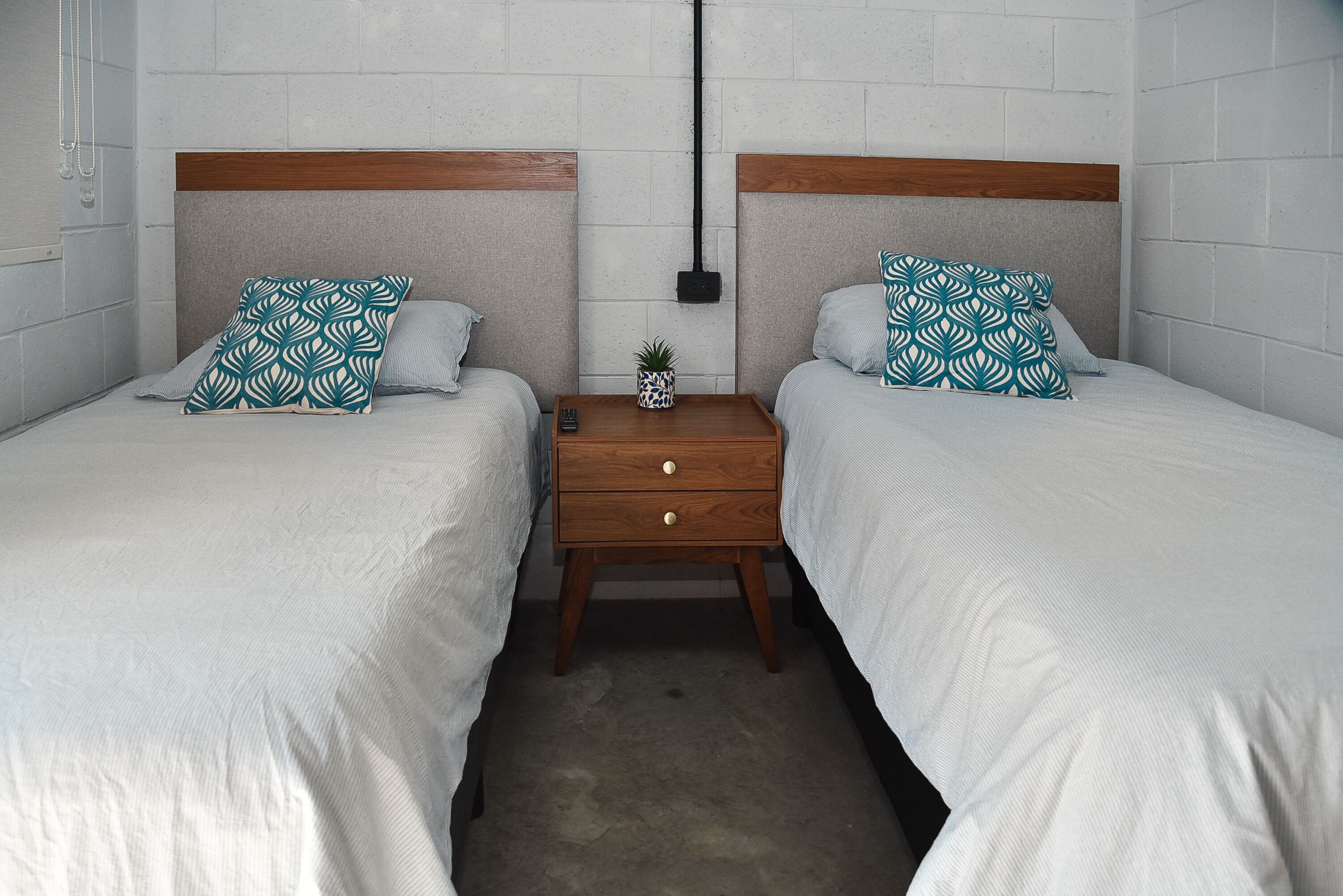 A twin room with two beds, each with a wooden headboard, a small bedside table with a plant, and a wall-mounted light fixture.