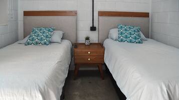 A twin room with two beds, each with a wooden headboard, a small bedside table with a plant, and a wall-mounted light fixture.