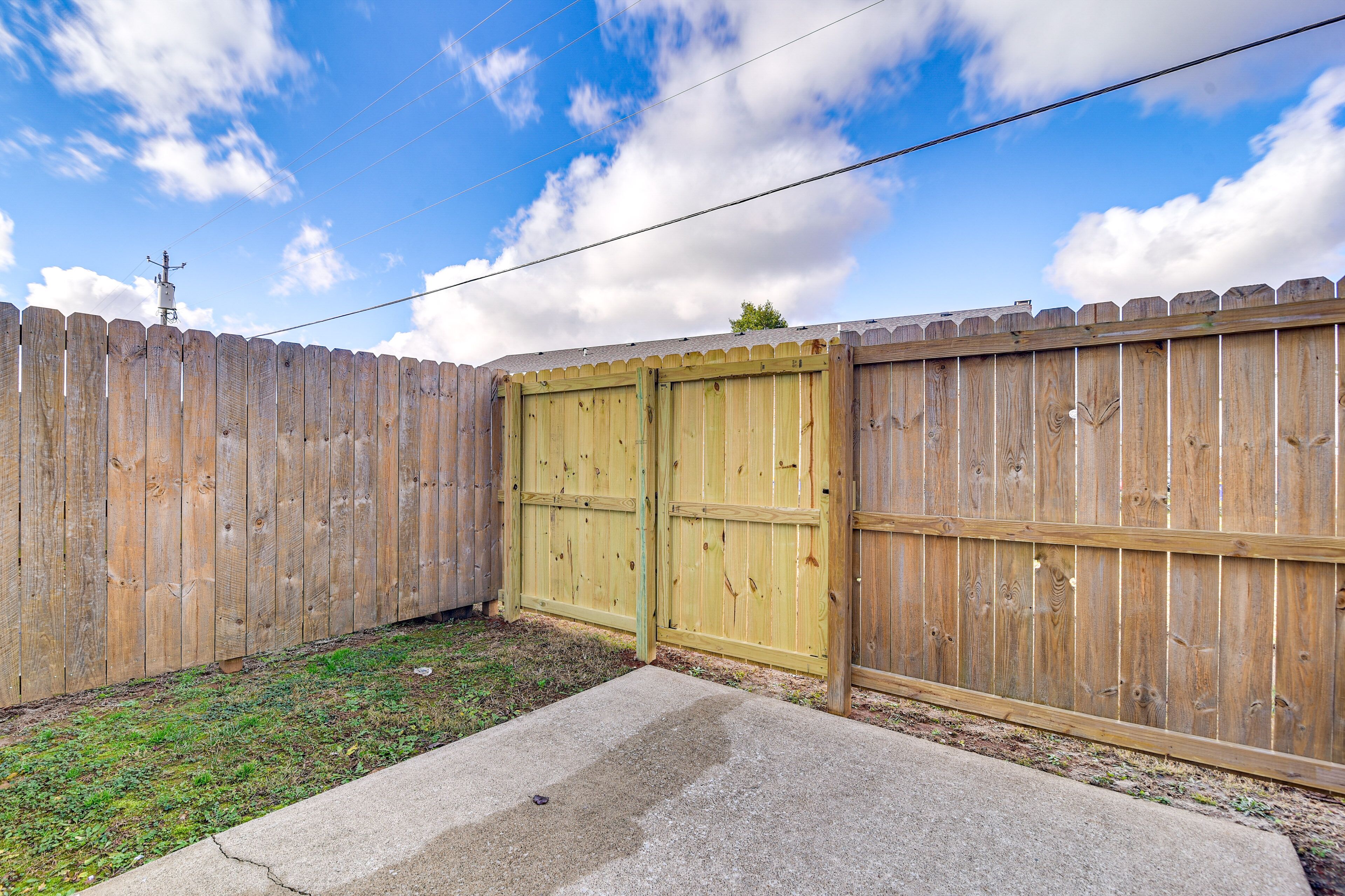 A wooden fence with a gate, a concrete patio, and a grassy area.