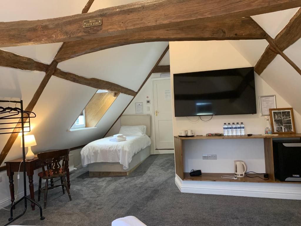Ein Schlafzimmer mit geneigter Decke, einem Bett, einem Schreibtisch mit Stuhl, einem an der Wand montierten Fernseher und einem Regal mit Gegenständen.