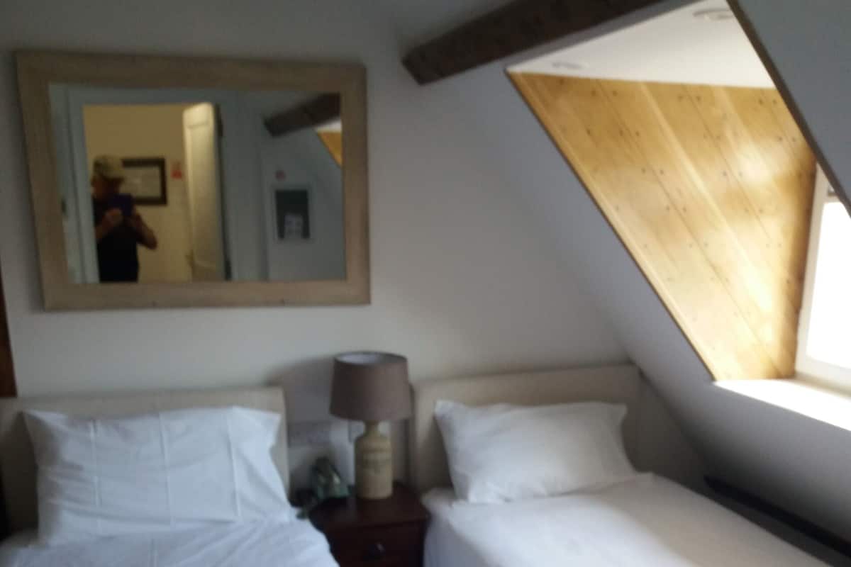 A hotel room with two beds, a mirror, a lamp, and a window with a wooden slat design.