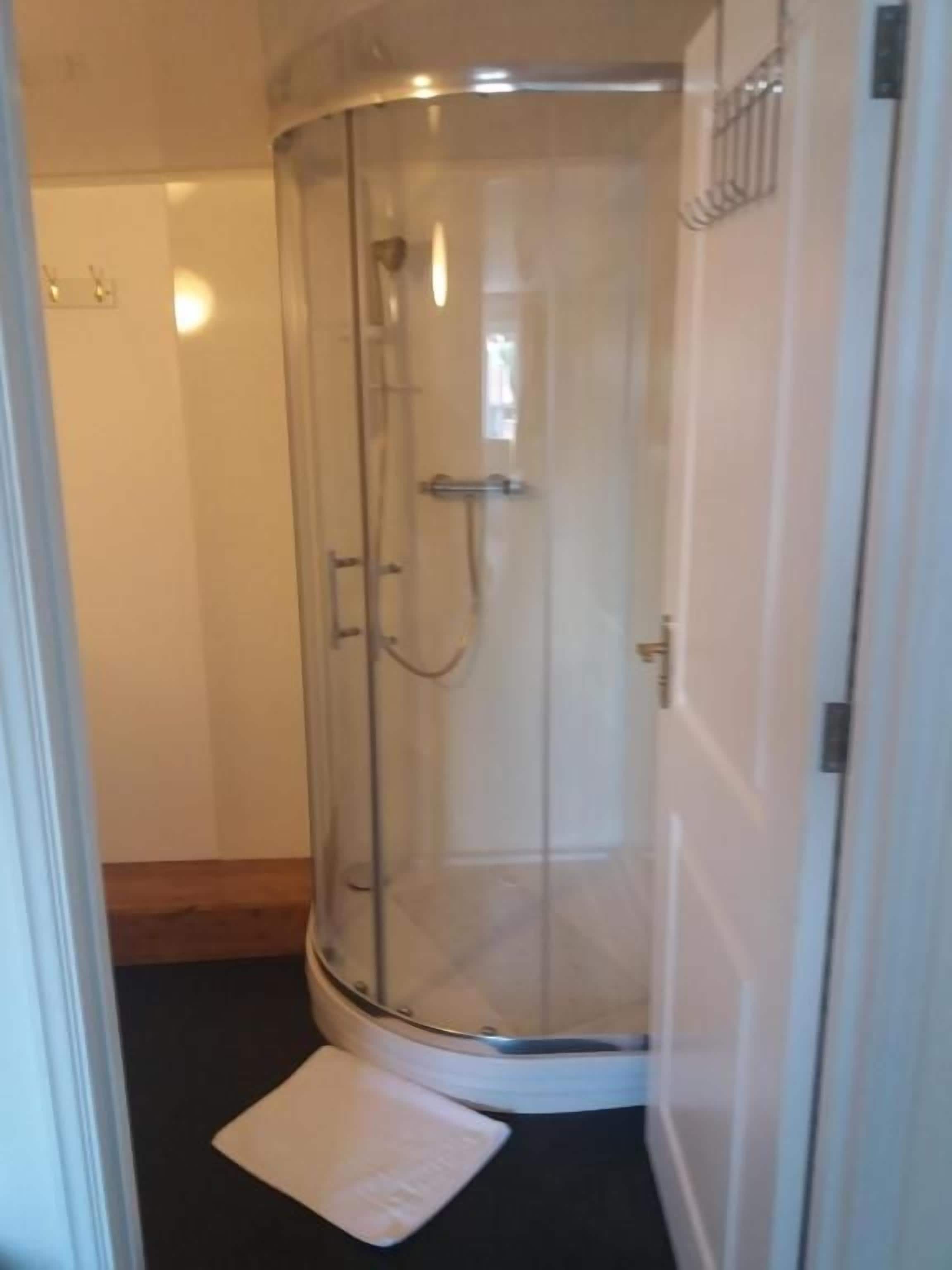 A glass-enclosed shower stall with a white mat at the base.