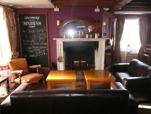 Una habitación con chimenea, una pizarra con información sobre eventos y un sofá de cuero.