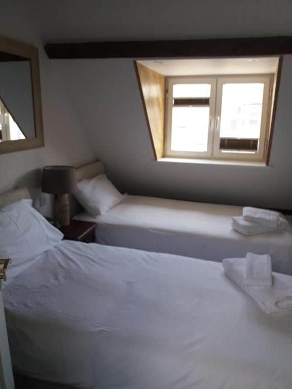 A room with two beds, a window, a lamp, and a mirror.