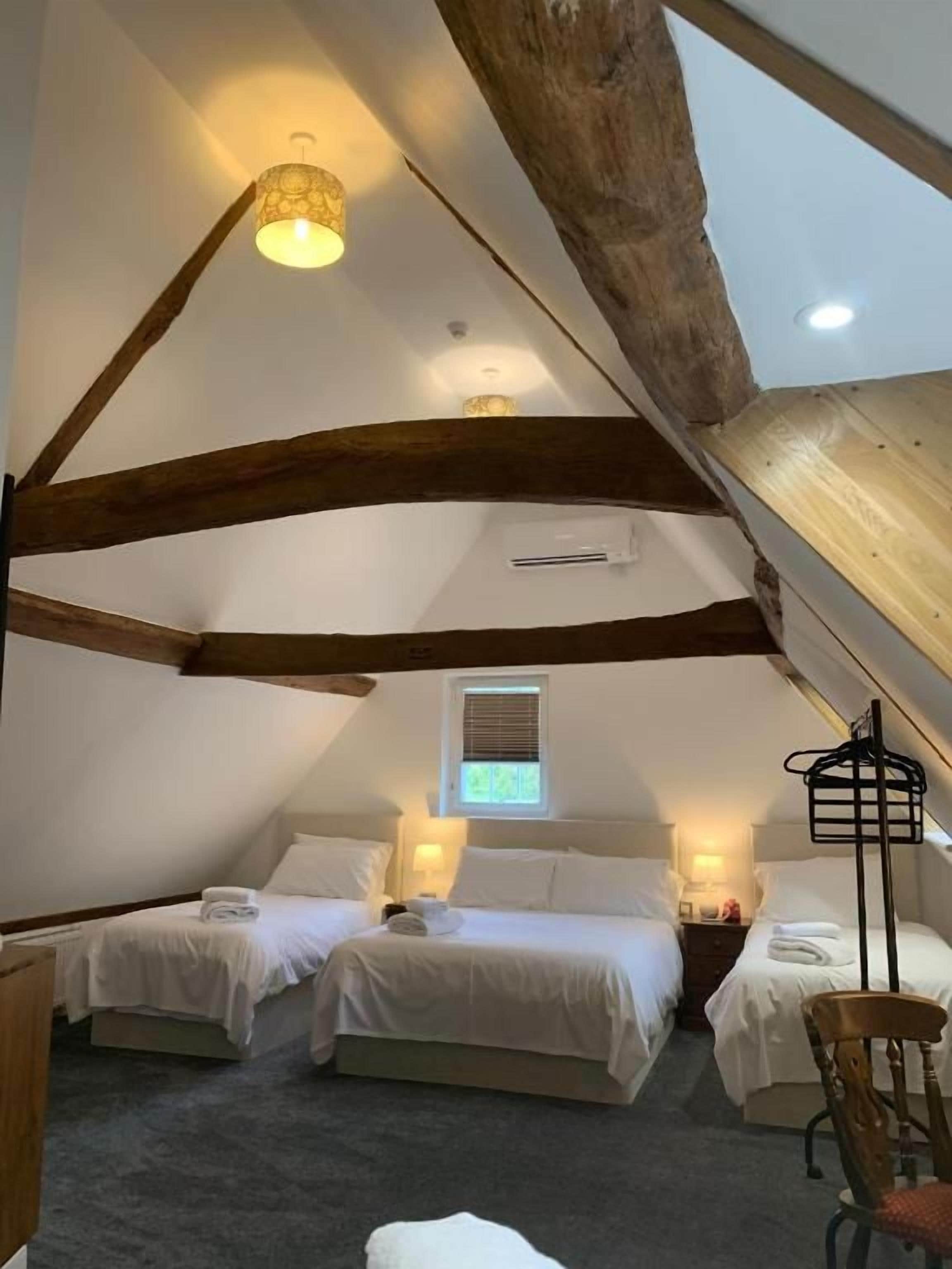 A room with two beds, a window, and a ceiling with exposed wooden beams.