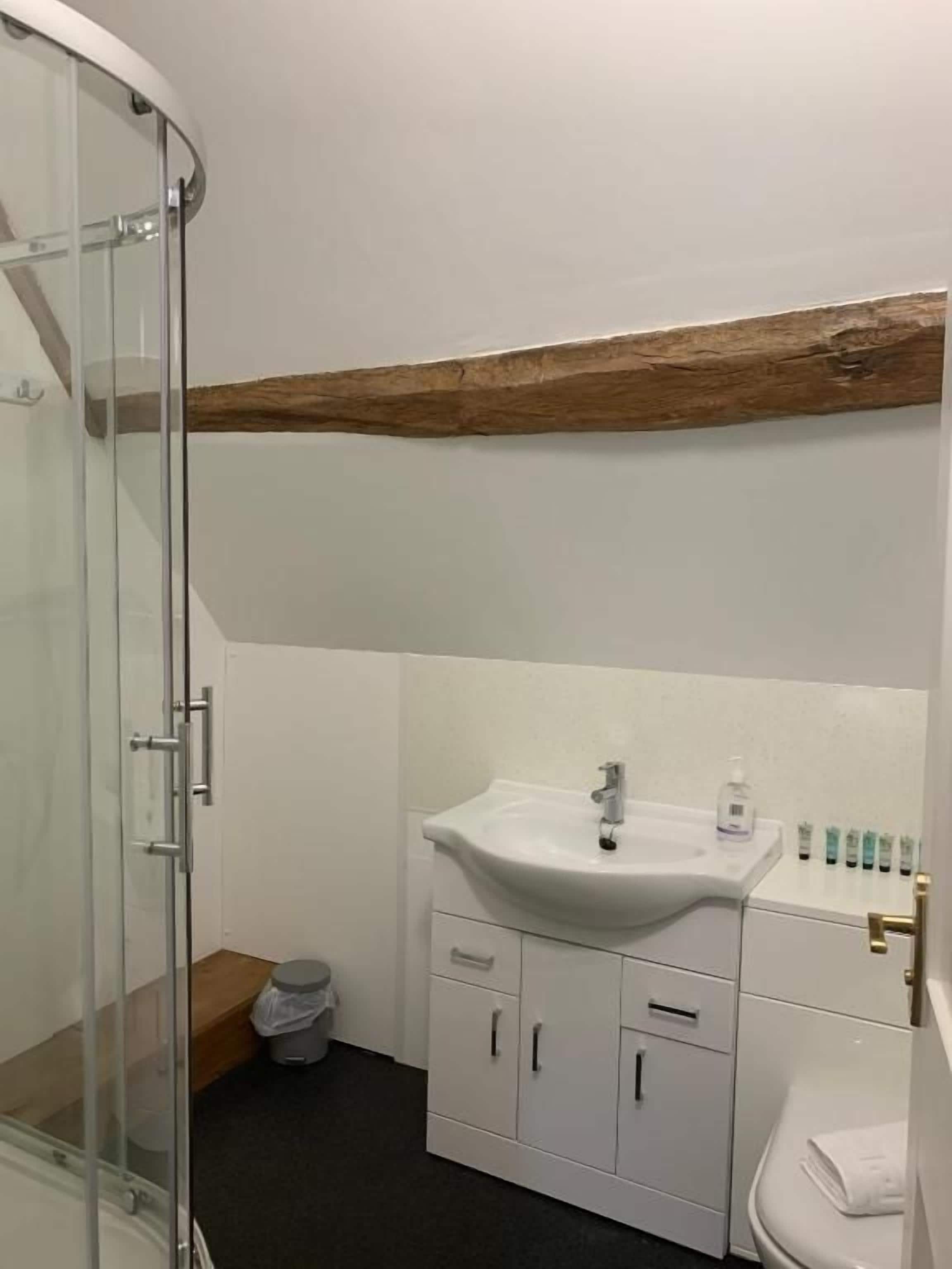A bathroom with a glass shower enclosure, a white sink with a mirror above, and a wooden beam above the sink.