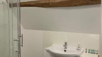A bathroom with a glass shower enclosure, a white sink with a mirror above, and a wooden beam above the sink.
