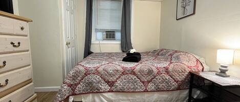 A bedroom with a bed, a dresser, a desk, and a window with curtains.