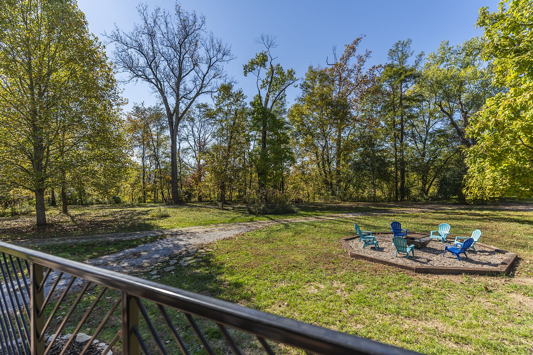 A park with a gravel path, green grass, and a wooden deck with Adirondack chairs.