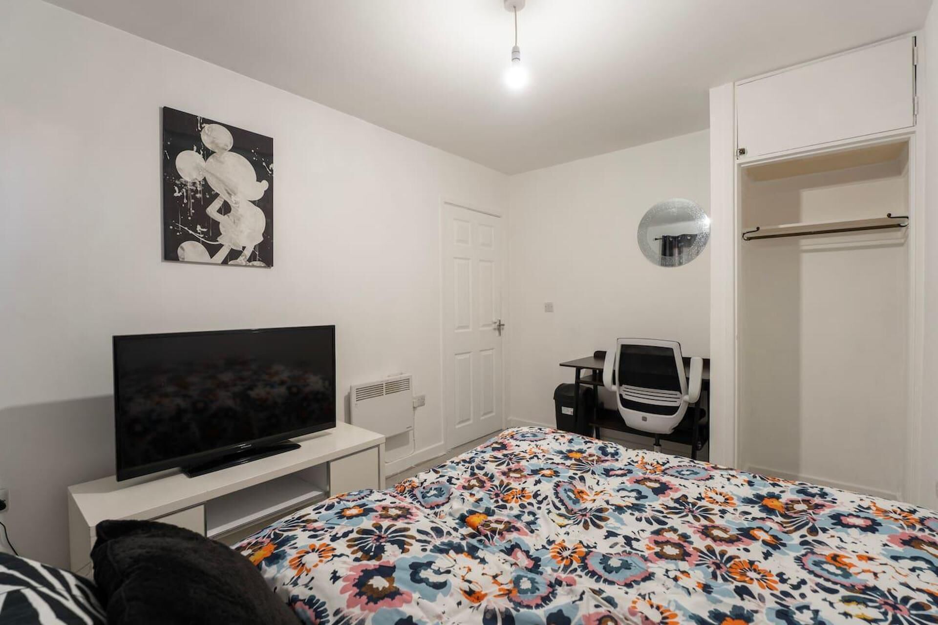 A bedroom with a bed, a TV, a desk, a chair, a wardrobe, and a mirror.