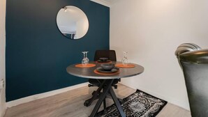 Ein Essbereich mit einem runden Tisch, zwei Stühlen, einem runden Spiegel an der Wand und einem gemusterten Teppich.