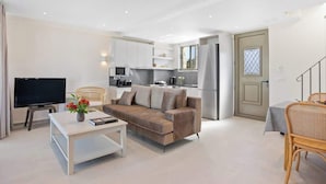 A modern living room with a sofa, coffee table, TV, and a kitchen area with cabinets and appliances. - Theseus Villa (Chania Town)