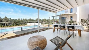 A modern outdoor dining area with a pool, large windows, and a view of the landscape. - Theseus Villa (Chania Town)