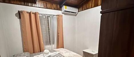 Een slaapkamer met een bed, een klein nachtkastje, een kledingkast en een airconditioner.