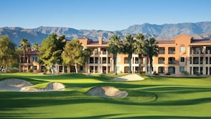 A golf course with bunkers and palm trees, surrounded by a multi-story building with a mountainous backdrop. - UNAVAILABLE    (Palm Desert)
