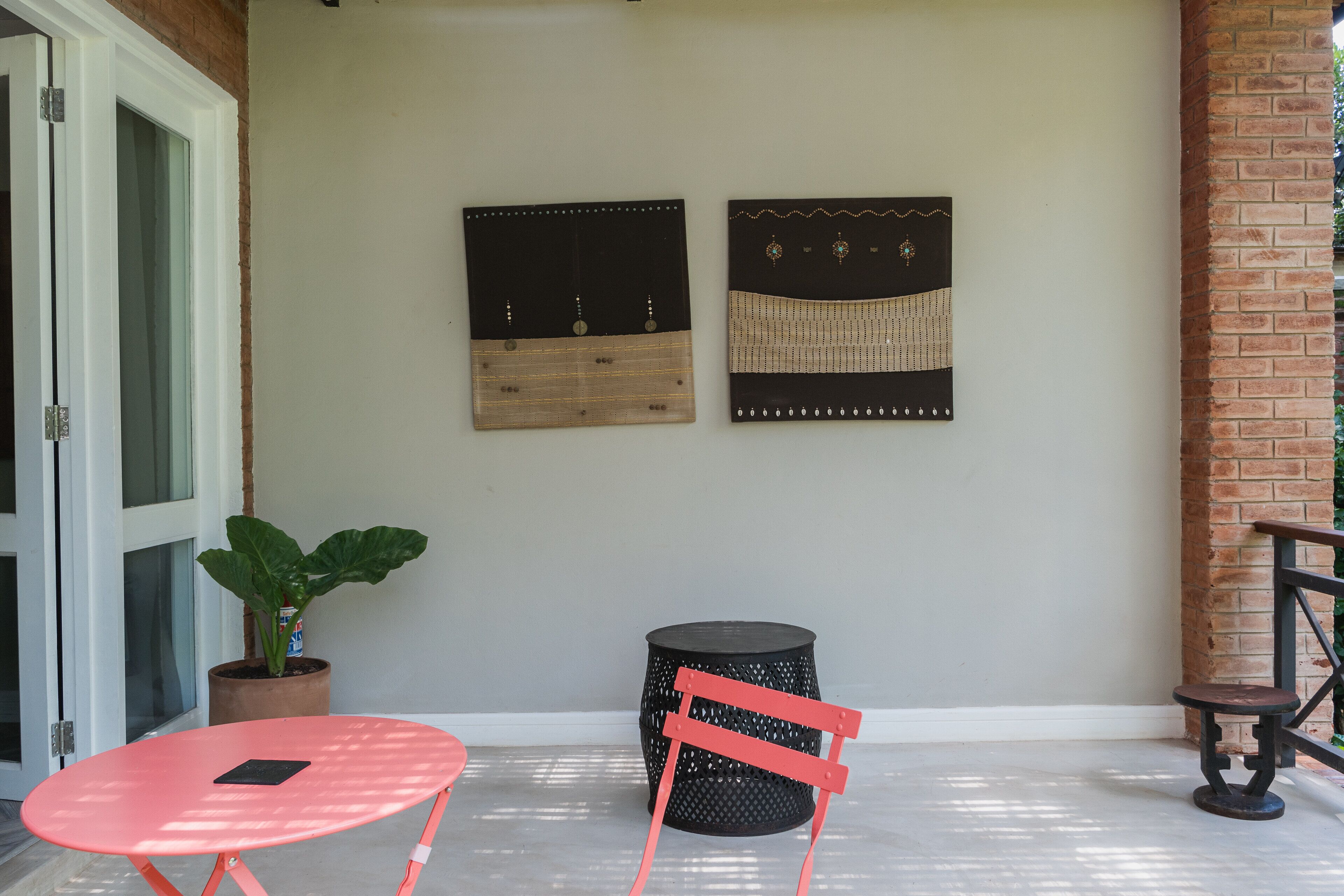 A small patio area with a red table and chair, a potted plant, and two wall-mounted decorative panels.